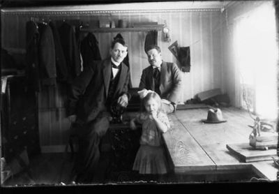 2 män och en flicka sittande vid skräddarbänk.
