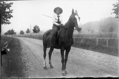 Kvinna sittande på häst.
Nyckelord: Häst Väg Dräkt