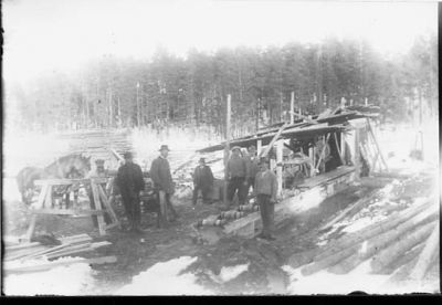 7 män stående vid sågverk.
Nyckelord: Häst