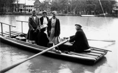 4 kvinnor rors med färja över kanalen. Byggnad i bakgrunden.
