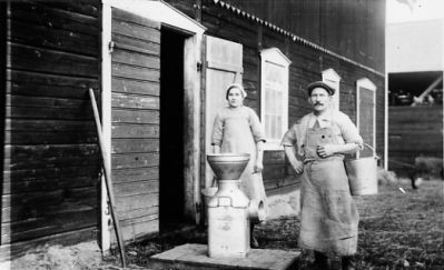 Man och kvinna stående på ladugårdsplan vid mjölkså.
Nyckelord: Mjölkså