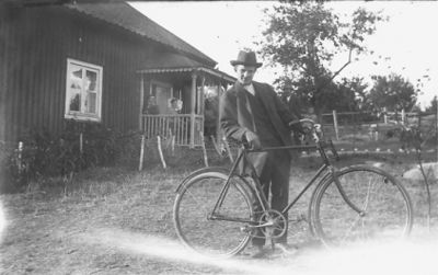 Man med cykel stående framför byggnad.
Nyckelord: Cykel