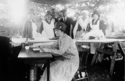 Ett antal personer stående bakom bord och 1 kvinna sittande vid bord.
