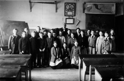 Skolklass med lärare stående för fotografering.
Nyckelord: Skolsal Skolbänkar