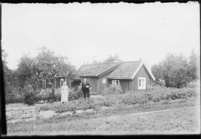 Man och kvinna stående i trädgård framför byggnad.
Nyckelord: Häck