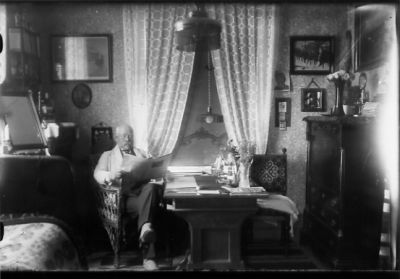 Man sittande vid bord med tidning.
Nyckelord: Gardiner