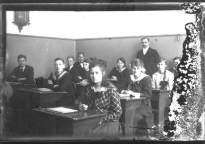 Skolelever sittande i sina bänkar och magistern stående längst bak.
Nyckelord: Skolsal