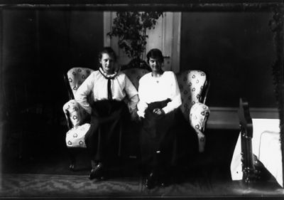 2 kvinnor sittande i soffa i rum.
Nyckelord: Soffa