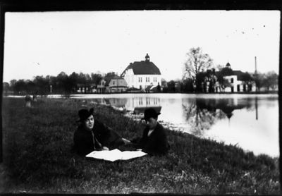 2 män sittande i gräset intill vattendrag.
