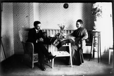 Man och kvinna sittande vid bord i rum.
Nyckelord: Blommor Pinnsoffa Korgfotölj Pedistal