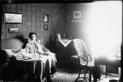 Kvinna sittande vid bord i rum.
Nyckelord: Blommor Tapet Tavla