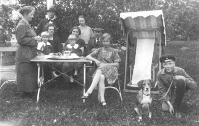 Familj sittande eller stående vid trädgårdsmöbel med kaffebricka.
Nyckelord: Hund Trädgårdsmöbel