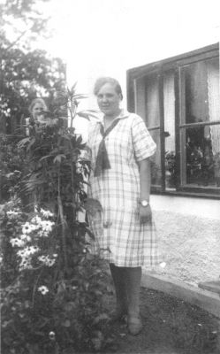 Kvinna stående framför fönster.
Nyckelord: Blommor Fönster Bostad