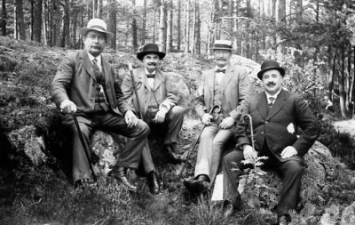 4 män sittande på sten i skogsbacke.
Nyckelord: Käpp Skogsbacke Skog Berg