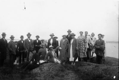 Ett antal personer stående eller sittande på berg med vatten i bakgrunden.
Nyckelord: Hav Berg
