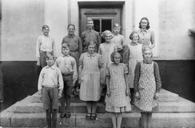 1 kvinna, 6 pojkar och 5 flickor stående på trappa till byggnad.
Nyckelord: Dörr Byggnad