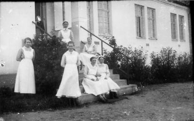 3 kvinnor sittande och 3 stående vid eller på trappa till byggnad.
Nyckelord: Trappa Uniform