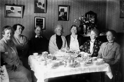 7 kvinnor sittande runt kaffebord i rum.
Nyckelord: Tavla Tapet