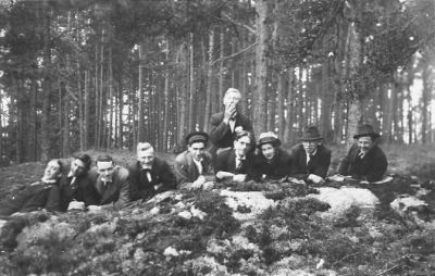 10 män sittande i skogsbacke.
Nyckelord: Skog