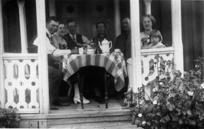 3 män, 3 kvinnor och 1 flicka sittande vid kaffebord på veranda.
Nyckelord: Trädgårdsmöbel Veranda