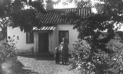 Kvinna och barn stående framför byggnad.
Nyckelord: Grusplan