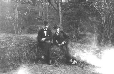 2 män sittande på sten.
Nyckelord: Skogsbacke Sten Träd Käpp