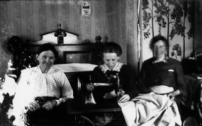 3 kvinnor sittande vid symaskin.
