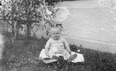 Barn sittande vid husvägg.
Nyckelord: Gräsmatta Husvägg