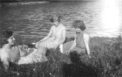 3 kvinnor sittande intill vattendrag.
Nyckelord: Gräsmatta