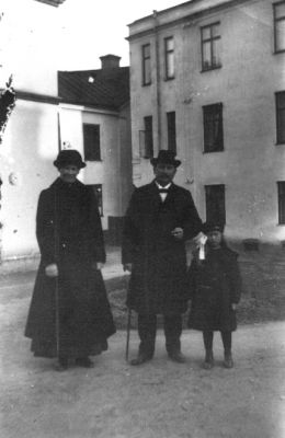 Man, kvinna och flicka stående framför byggnad.
Nyckelord: Käpp Gårdsplan