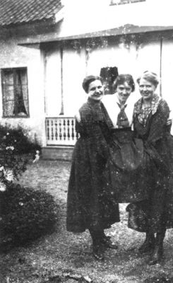 2 kvinnor bärande på kvinna framför byggnad.
Nyckelord: Gårdsplan Veranda