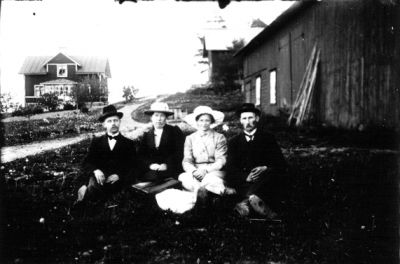 3 män och 1 kvinna sittande framför byggnad.
Nyckelord: Ekonomibyggnad