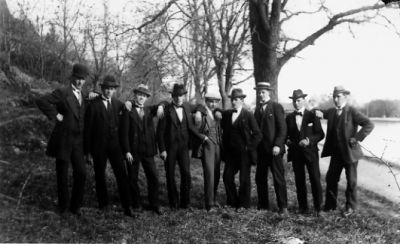 9 män stående intill vattendrag.
Nyckelord: Stig Träd