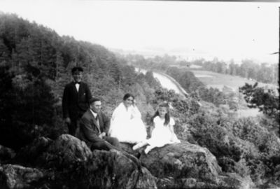 Man stående, man, kvinna och flicka sittande på berg med vattendrag i bakgrunden.
Nyckelord: Utsikt