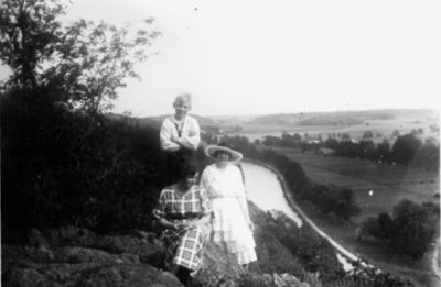 Kvinna och pojke stående, kvinna sittande på berg med vattendrag i bakgrunden.
Nyckelord: Utsikt