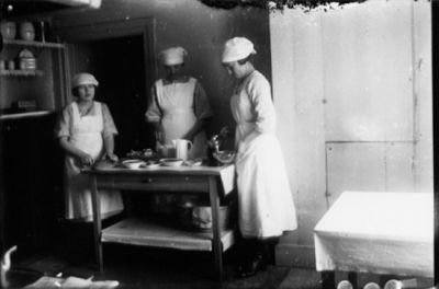 3 kvinnor stående i rum.
Nyckelord: Dräkt Köksredskap