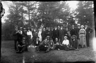 Ett antal personer sittande eller stående i naturen.
Nyckelord: Fiol Picnickorg