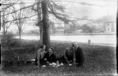 2 män och 2 kvinnor sittande på gräset intill vattendrag med picnickorg.
Nyckelord: Picnickorg