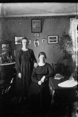 Kvinna sittande och kvinna stående i rum.
Nyckelord: Tavla Spegel