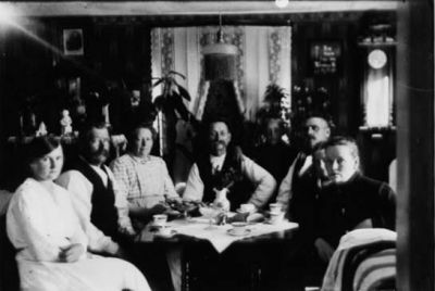 3 män, 3 kvinnor, pojke och flicka sittande runt kaffebord.
Nyckelord: Kaffebord Lampa Gardin