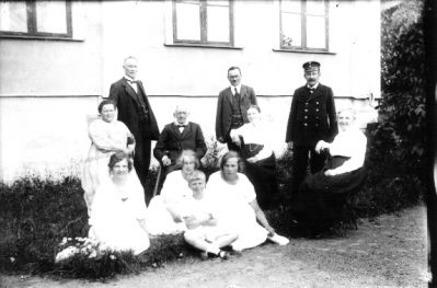 3 män stående, man, 6 kvinnor och pojke sittande framför byggnad.
Nyckelord: Uniform