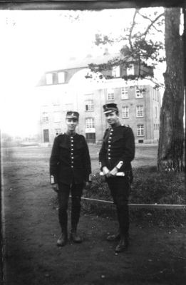 2 uniformerade män stående vid träd framför byggnad.
Nyckelord: Uniform Byggnad