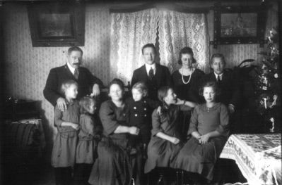 Familj sittande eller stående i rum.
Nyckelord: Julgran Tavla Gardin