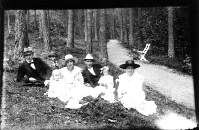 3 män, 2 kvinnor och 2 flickor sittande i skogsbacke.
Nyckelord: Skogsbacke Parkbänk