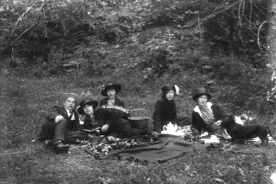 Man och 4 kvinnor sittande på filt i skogsbacke.
Nyckelord: Picnickorg Dragspel Filt