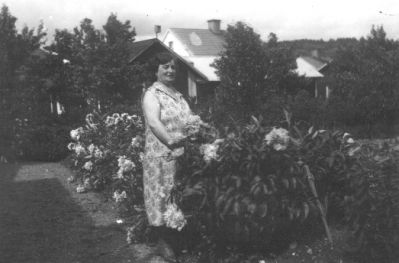 Kvinna stående i trädgård.
Nyckelord: Blommor Bostad