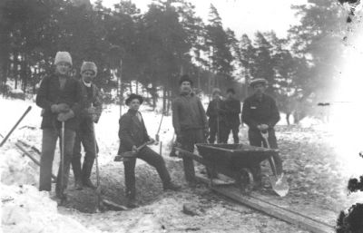 8 män stående med verktyg och skottkärra.
Nyckelord: Vinter Skottkärra Spade