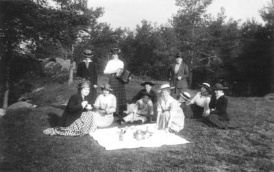 10 kvinnor och 1 flicka sittande eller stående runt picnicfilt.
Nyckelord: Picnic Dragspel