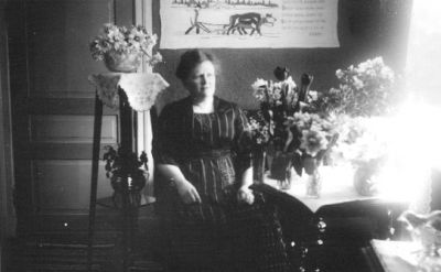 Kvinna sittande i rum med blommor.
Nyckelord: Blommor Väggbonad Pedistal
