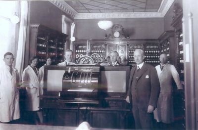 5 män och 2 kvinnor i apotek
Nyckelord: Kassaapparat Medicinburk Väggklocka Takmålning Stuckatur